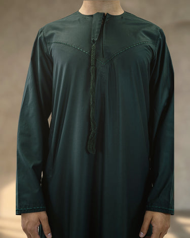 A man wearing a dark green Emirati kandura with a matching braided tassel and chevron embroidered chest trim.