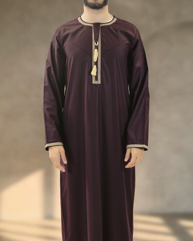 Front view of a man wearing a deep plum Emirati kandura with cream embroidered trim and a traditional tassel.