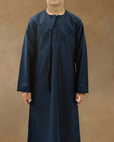 Young boy wearing the Little Hatta navy blue Emirati thobe with traditional hanging chest tassel and tonal embroidery.