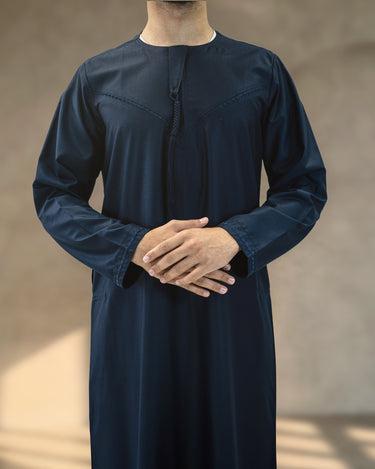 Front view of a man wearing a deep navy blue Emirati thobe with a braided tassel and chest embroidery.