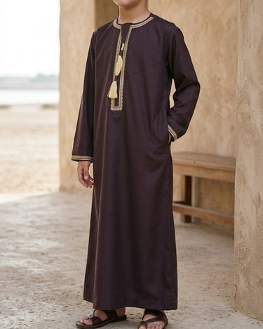 Little Ajman Kandura – Boys' Plum Tassel Emirati Thobe, walking toward camera, thobe wala signature · warm plaster interior – Thobe Wala