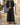 Little Al Ain Kandura – Boys' Black Tassel Emirati Thobe, walking toward camera, mediterranean · whitewashed finca, blue door – Thobe Wala