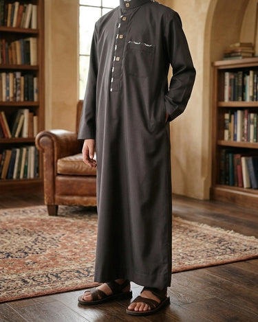 Little Baha Thobe – Boys' Black Trimmed Saudi Thobe, walking toward camera, rl heritage · wood-panelled library – Thobe Wala